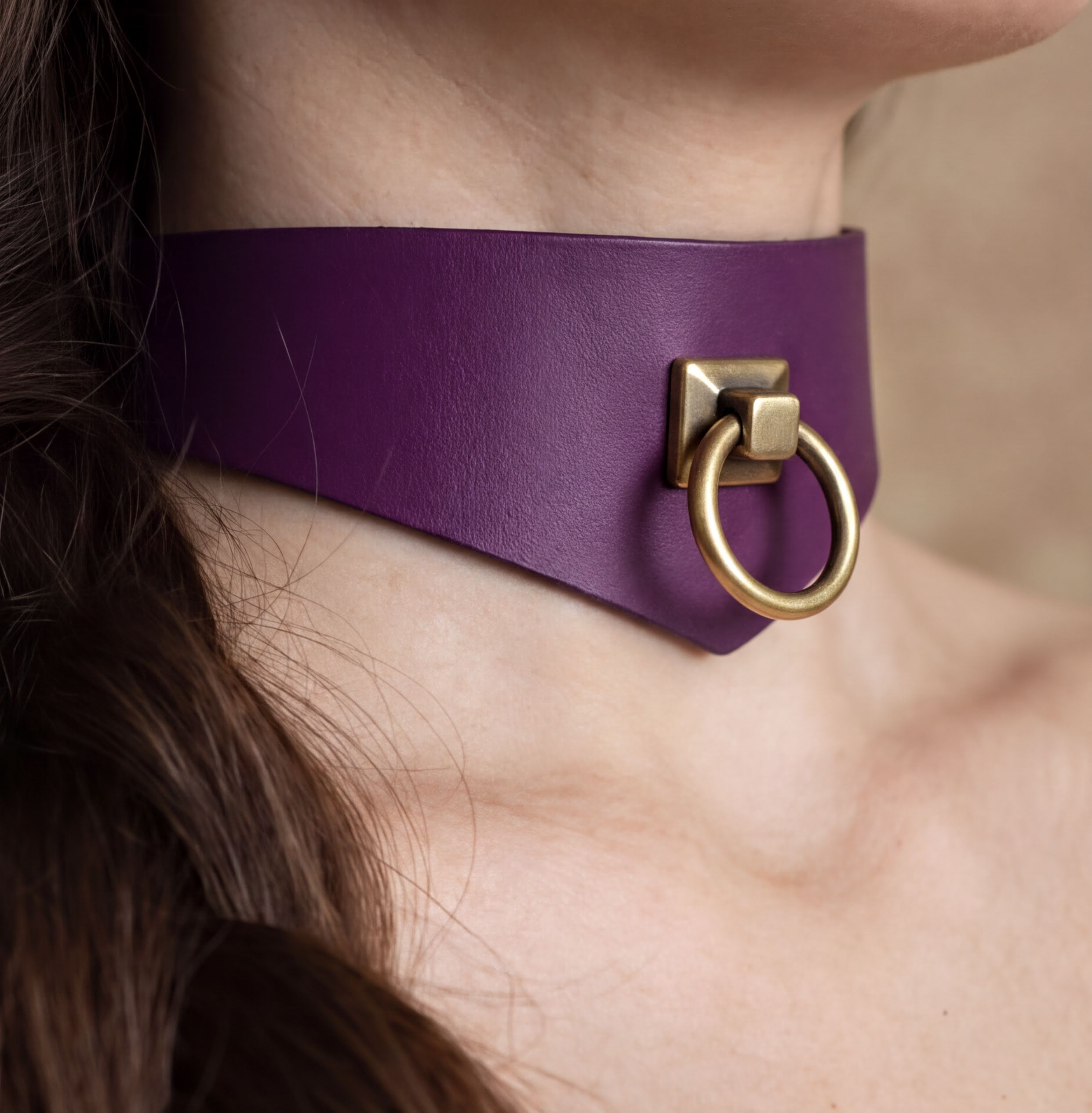 A close-up view of a person's neck and chin area, featuring a purple choker necklace with a gold-colored metal ring.