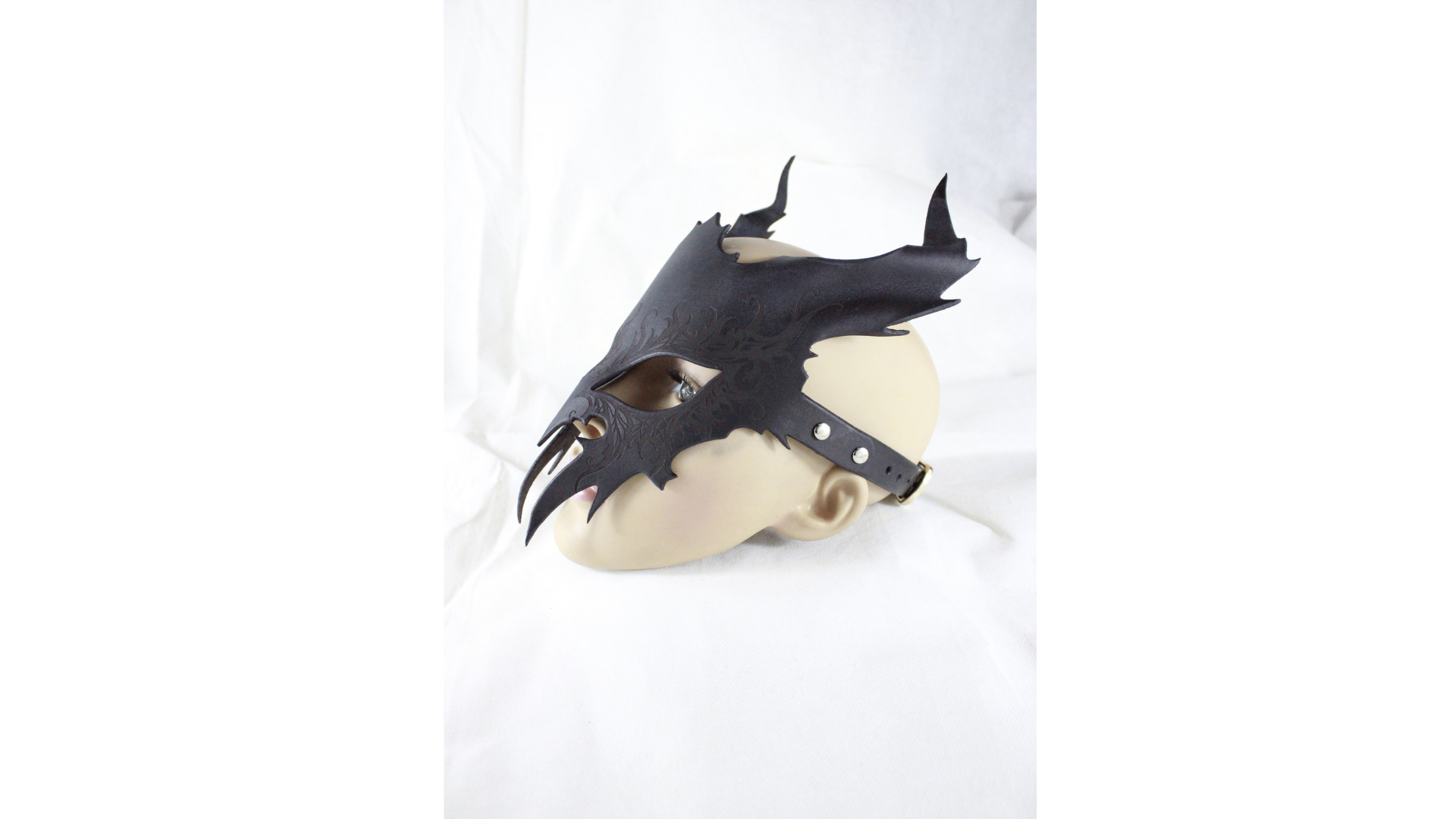 A black dragon mask with sharp teeth and claws is displayed against a white background.