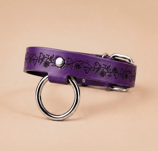A purple leather collar with a silver ring and floral design on it.