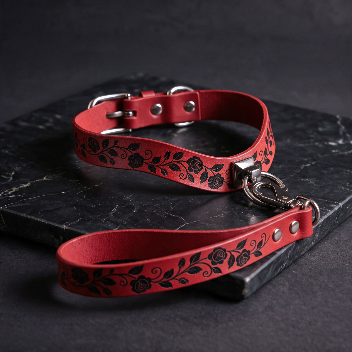 A red leather collar with a floral pattern and a matching leash is displayed on a black surface.