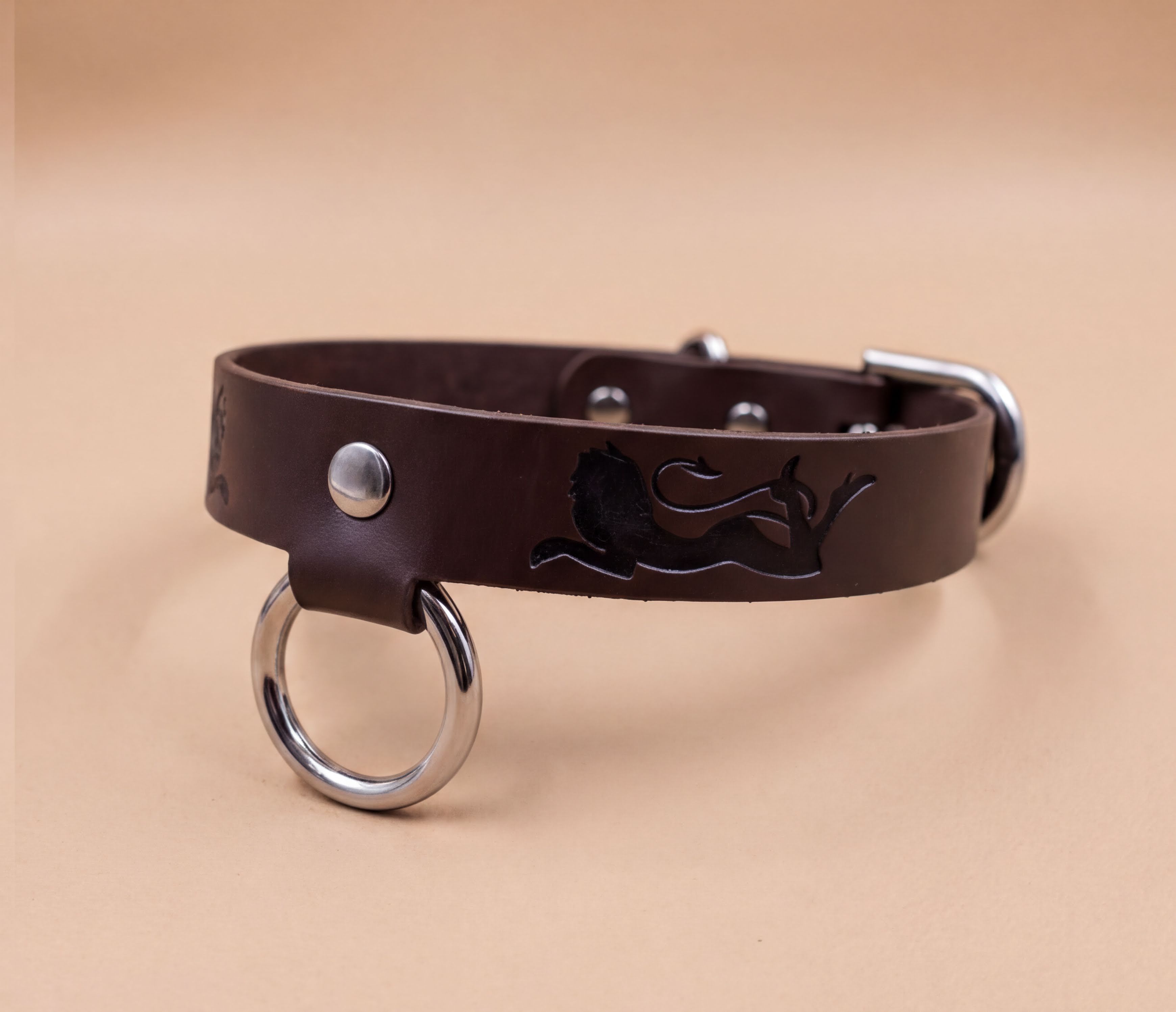 A brown leather dog collar with a metal ring and a lion design on it.