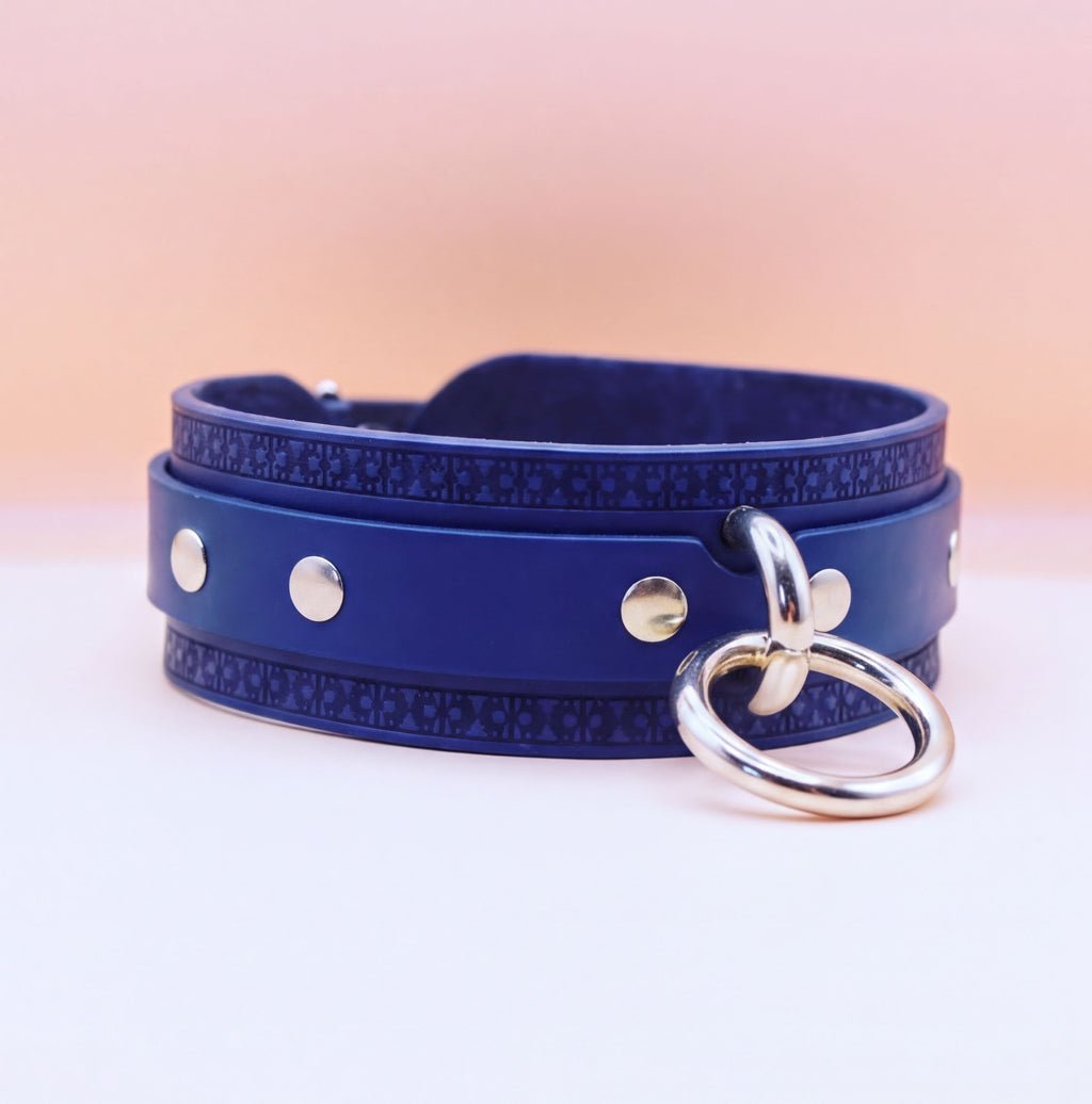 A blue leather choker necklace with silver metal rings and a silver ring hanging from it.
