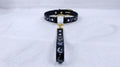 A black leather collar with a gold-colored buckle and a black strap with white designs.