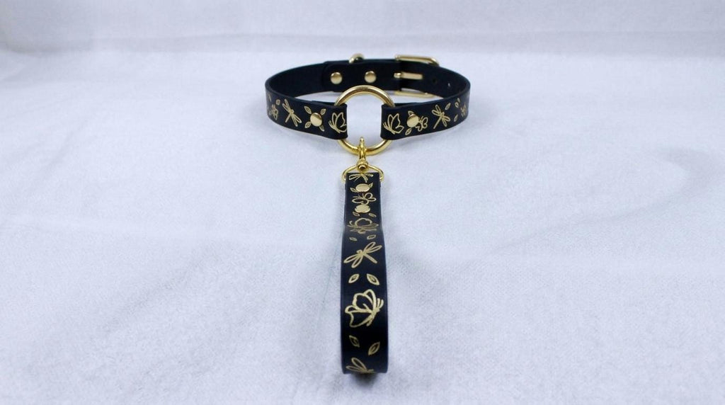 A black collar with gold floral designs and a gold-colored tag hanging from it.