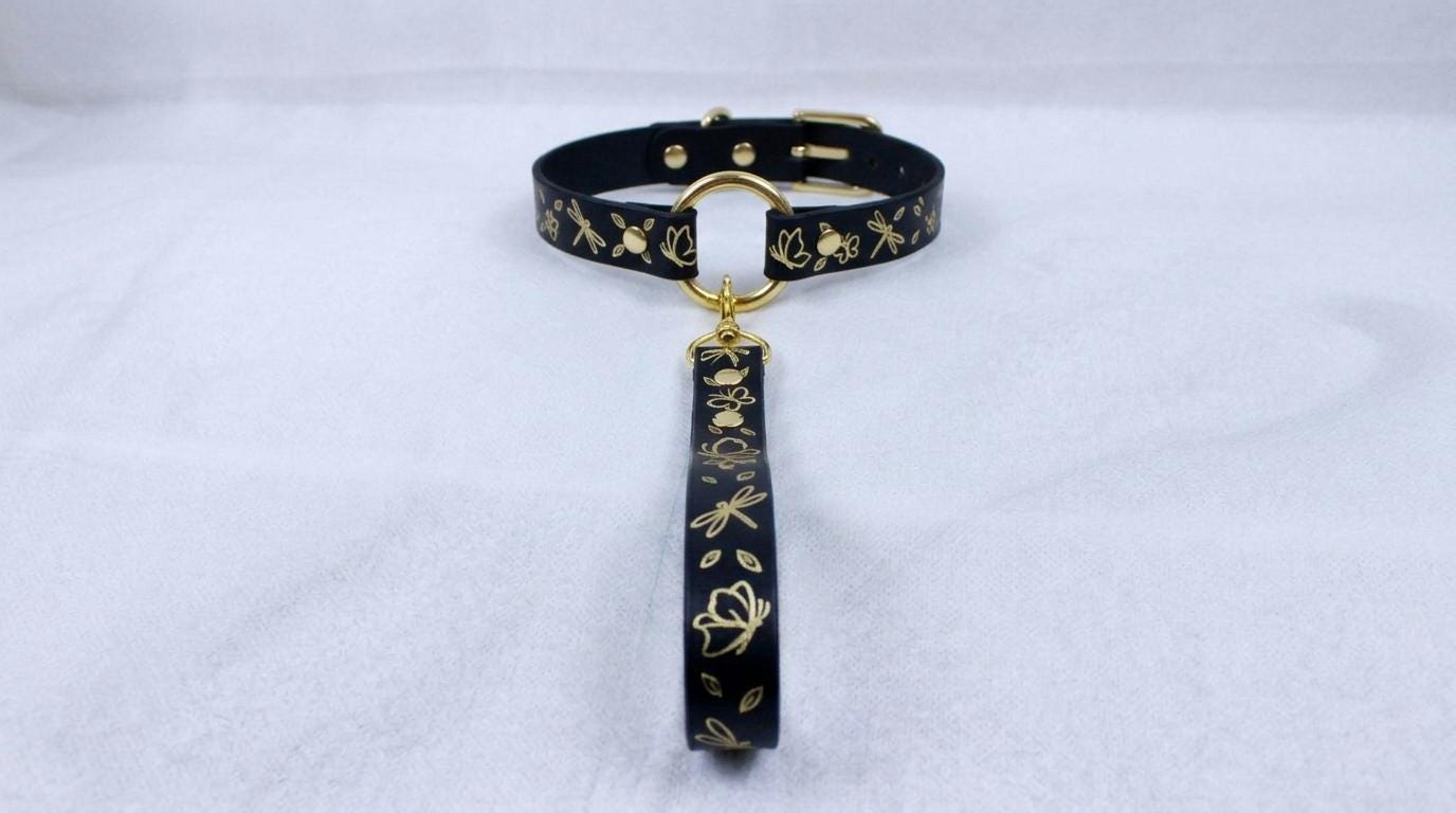 A black collar with gold floral designs and a gold-colored tag hanging from it.