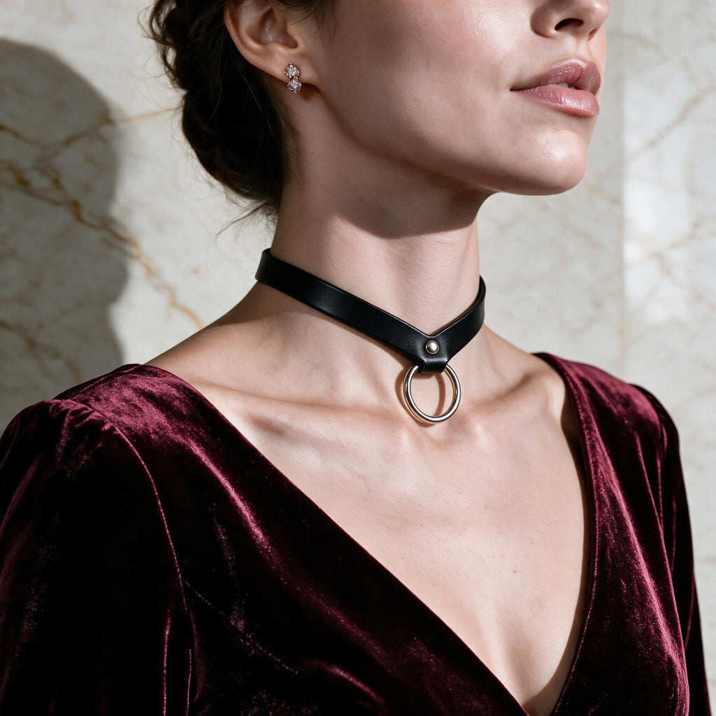 A woman wearing a black choker necklace with a silver ring on it, wearing a burgundy velvet dress.