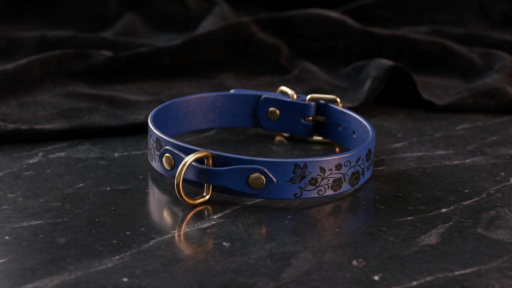 A blue leather collar with a floral design and gold hardware is displayed on a black marble surface.