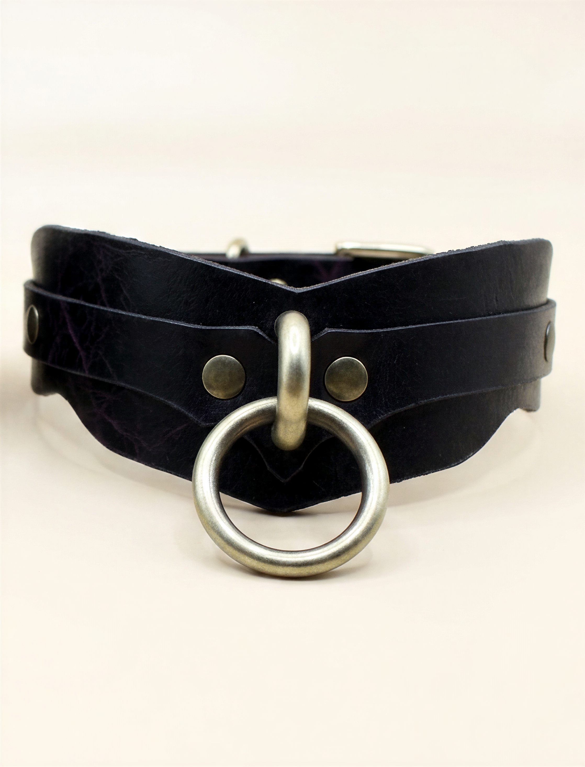 A black leather choker necklace with a metal ring and two metal clasps.