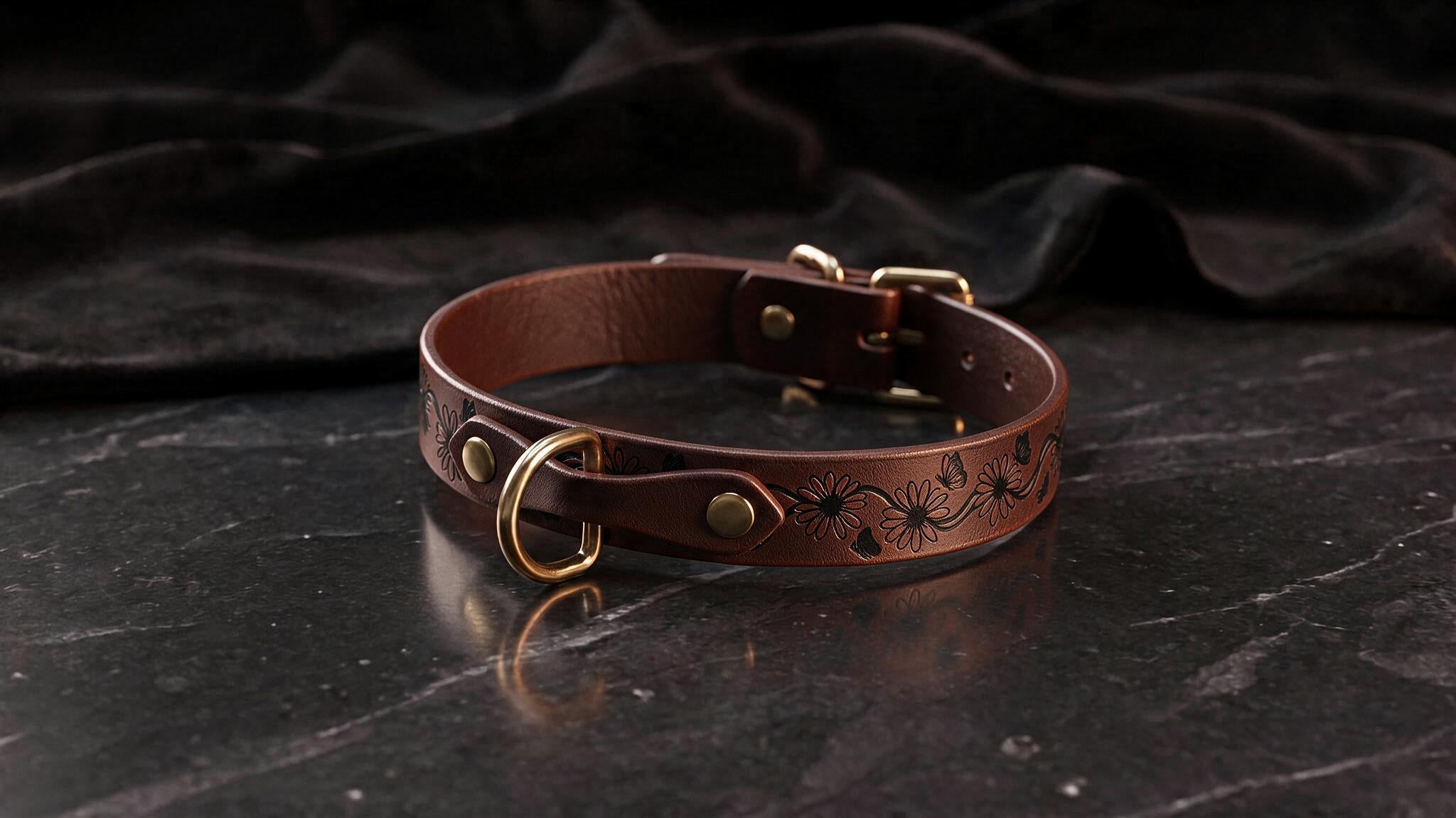 A brown leather collar with a floral design sits on a dark surface.