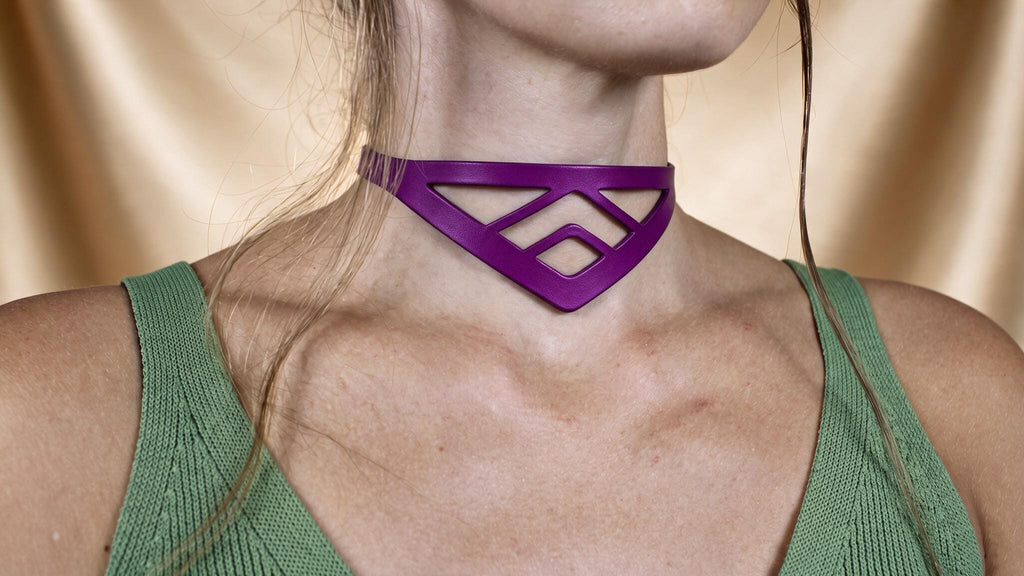 A close-up of a woman wearing a green top and a purple choker necklace with a geometric pattern.