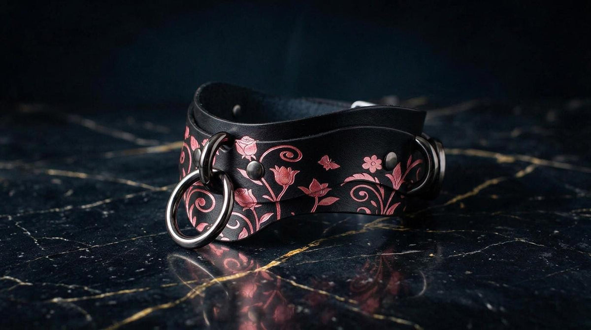 A black leather choker necklace with a floral pattern and metal rings is displayed on a dark marble surface.