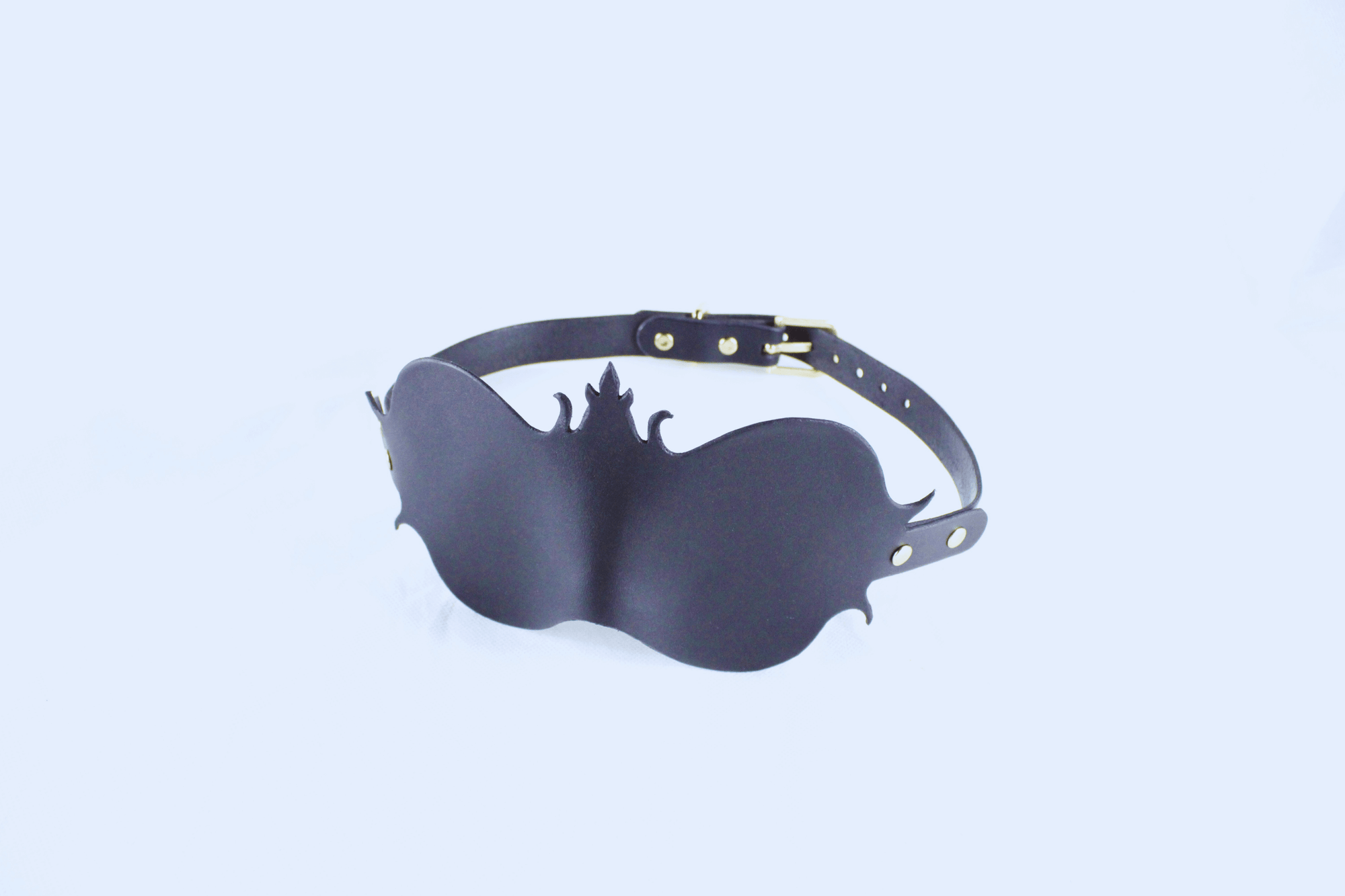 A black leather mask with a decorative design on the strap and a gold buckle.
