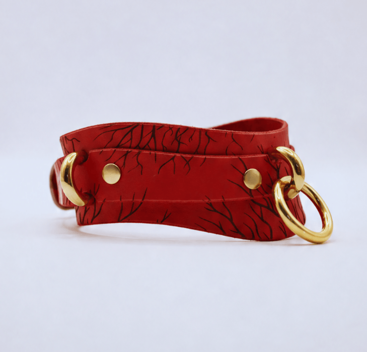 A red leather strap with a black leaf pattern and two gold-colored metal rings on either side.