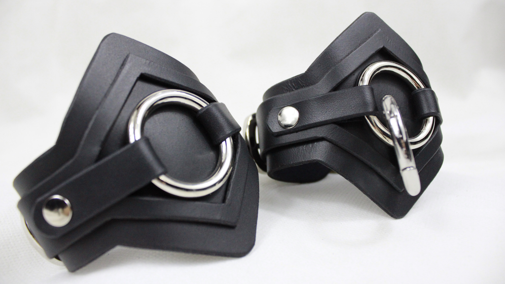 A pair of black leather cuffs with metal rings and buckles.