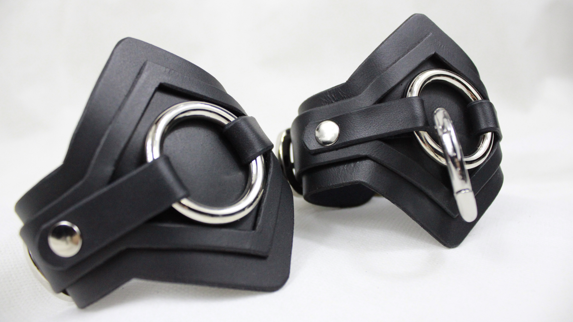 A pair of black leather cuffs with metal rings and buckles.