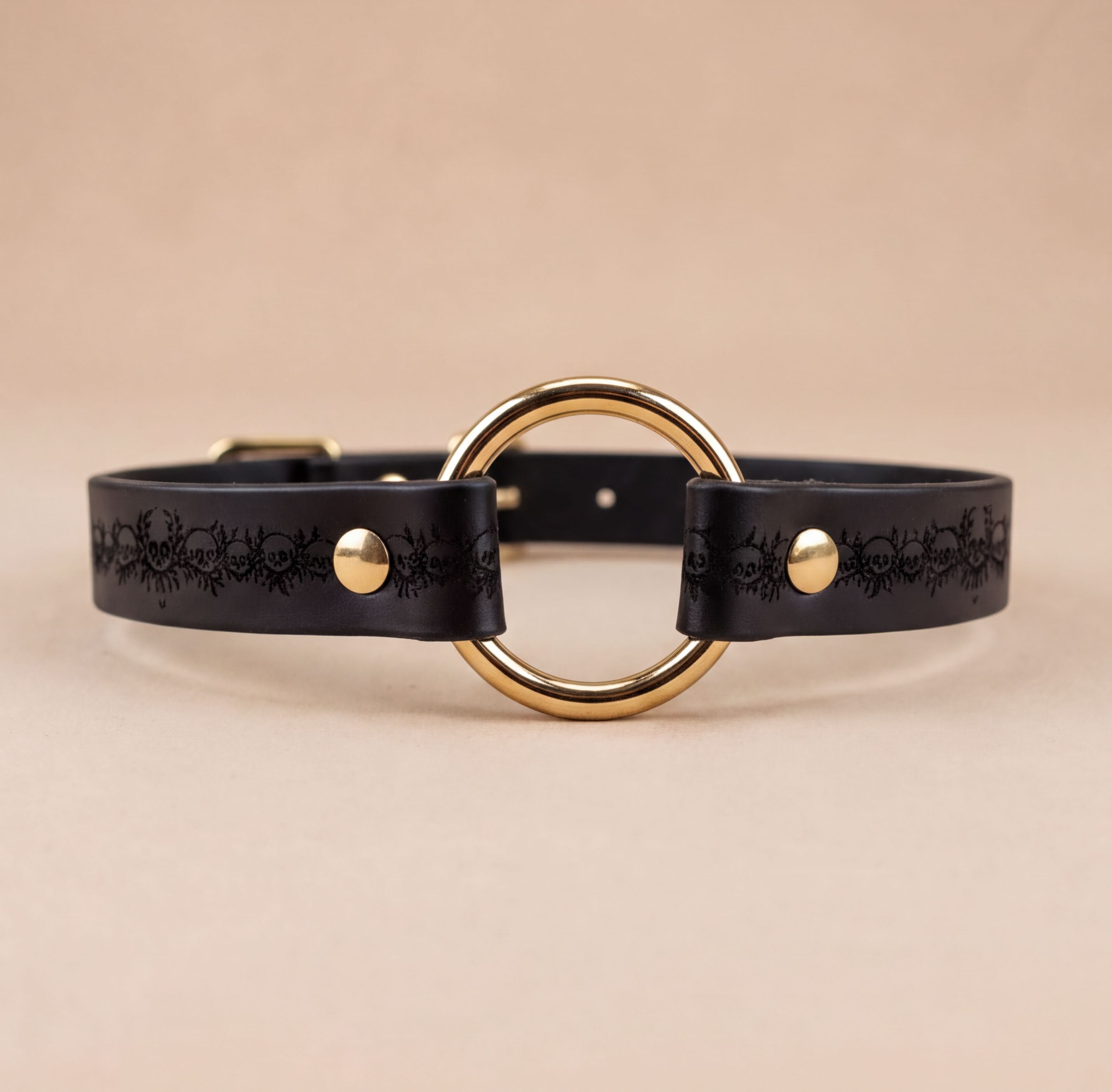 A black leather choker necklace with a gold-colored circular buckle.