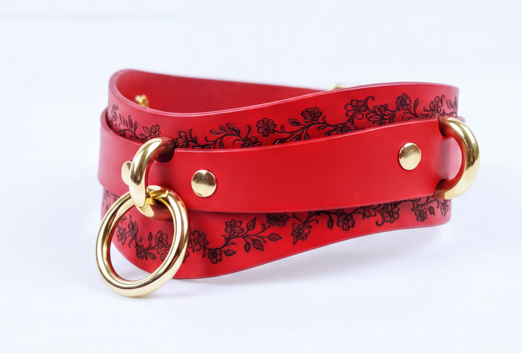 A red leather strap with a floral pattern and two gold-colored metal rings on the ends.
