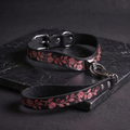 A black leather collar with a floral pattern and a matching leash attached to it, resting on a dark surface.