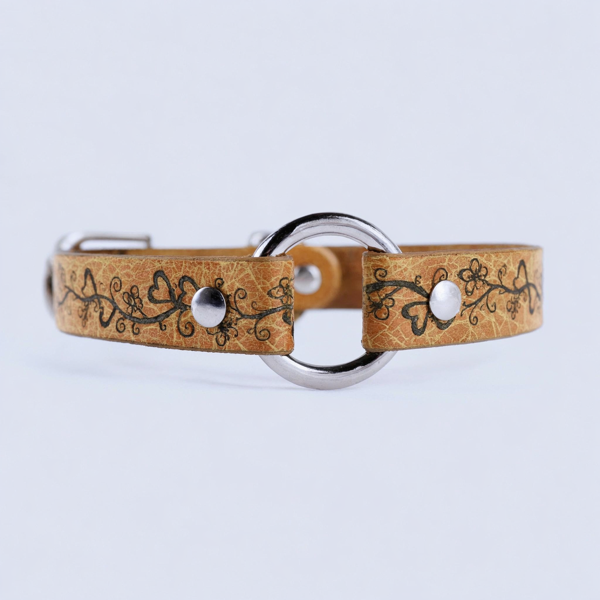 A tan leather collar with a floral design and metal ring, featuring two silver buttons.