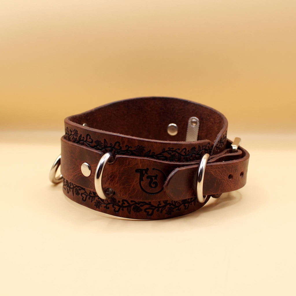 A brown leather collar with metal rings and a decorative pattern on the surface.