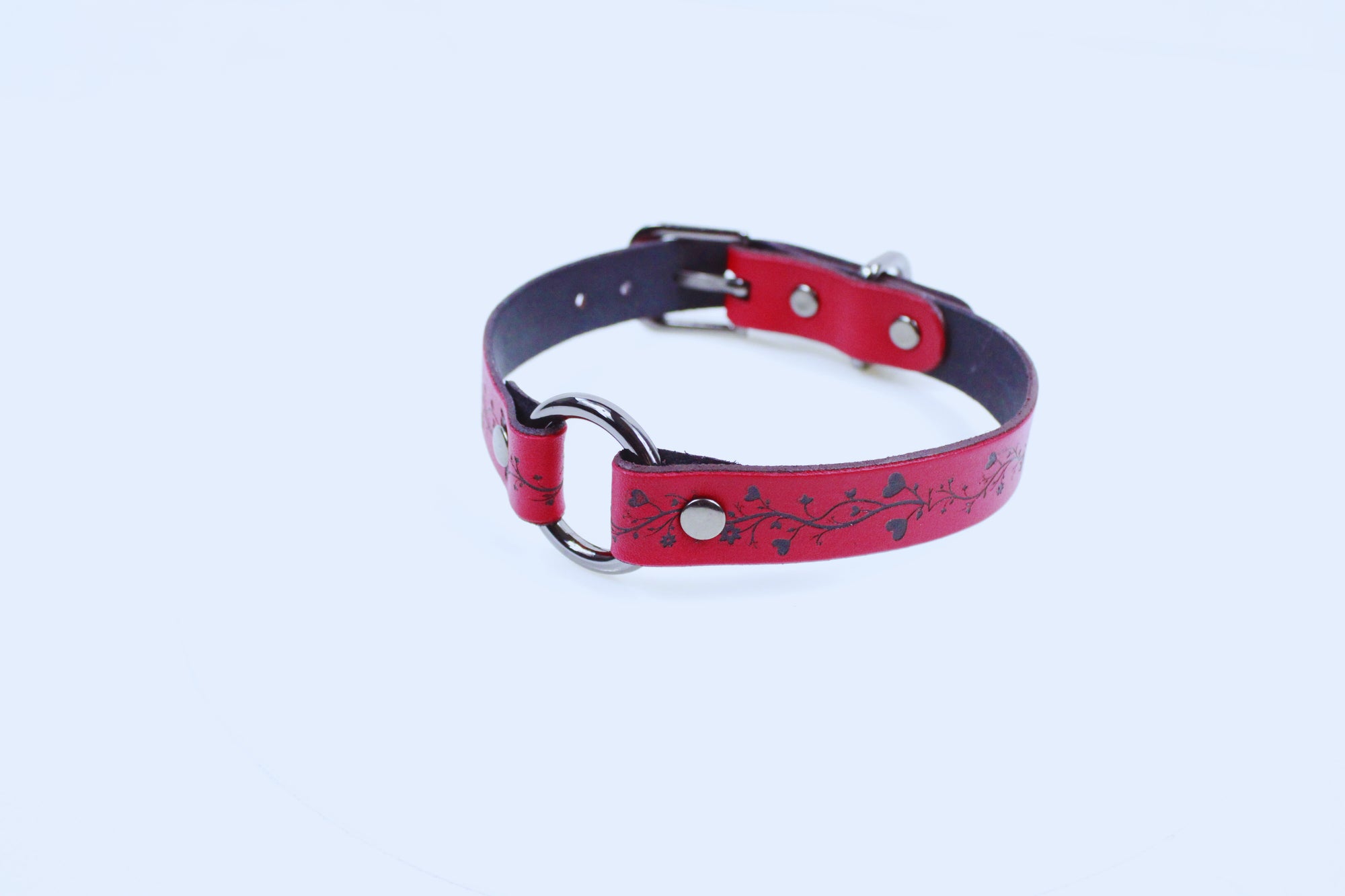 A red leather dog collar with metal rings and a decorative pattern on the strap.
