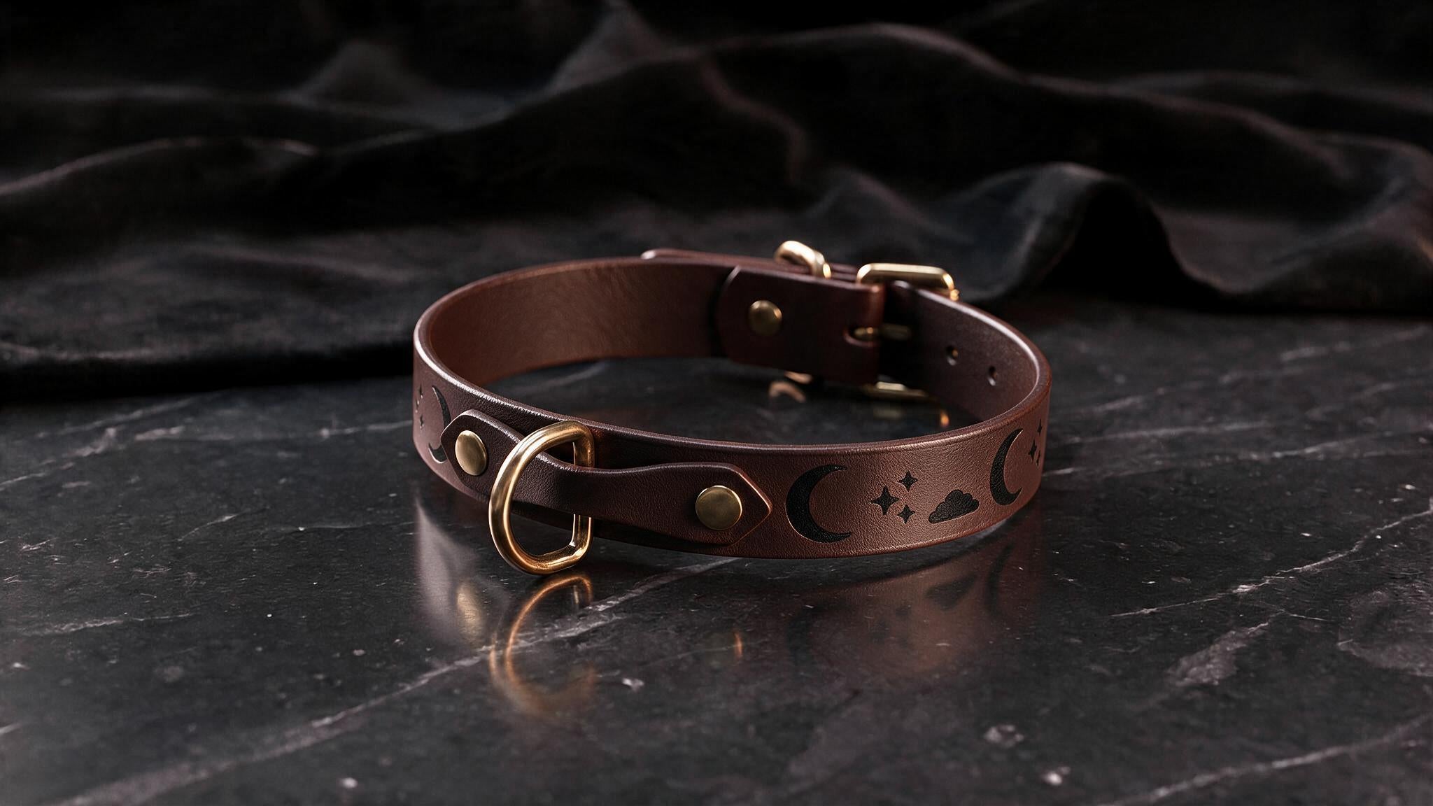 A brown leather collar with a moon and star design on it, resting on a dark surface.