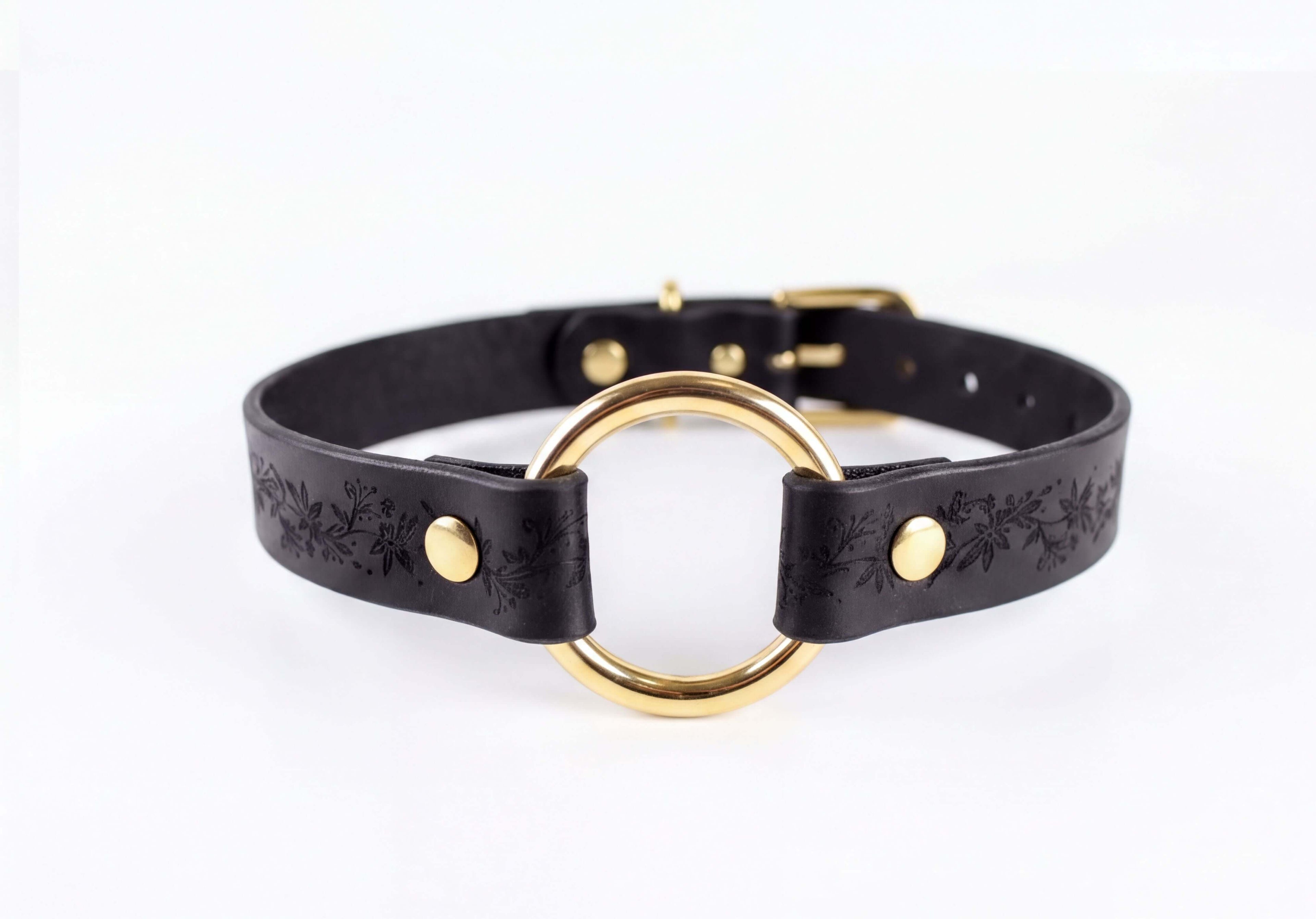 A black leather choker collar with a gold-colored circular buckle.