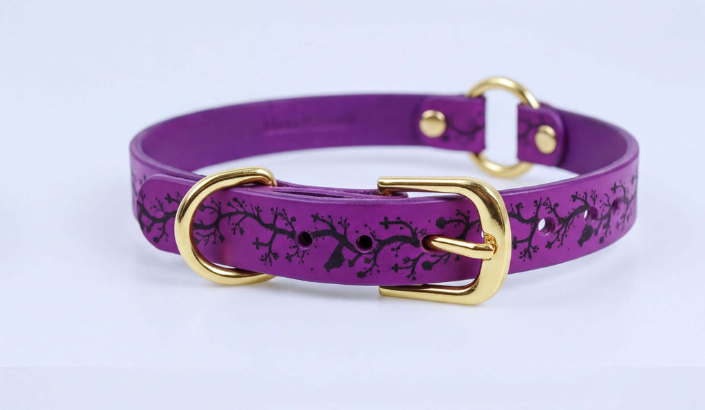 A purple leather dog collar with a gold buckle and a black tree design on the front.