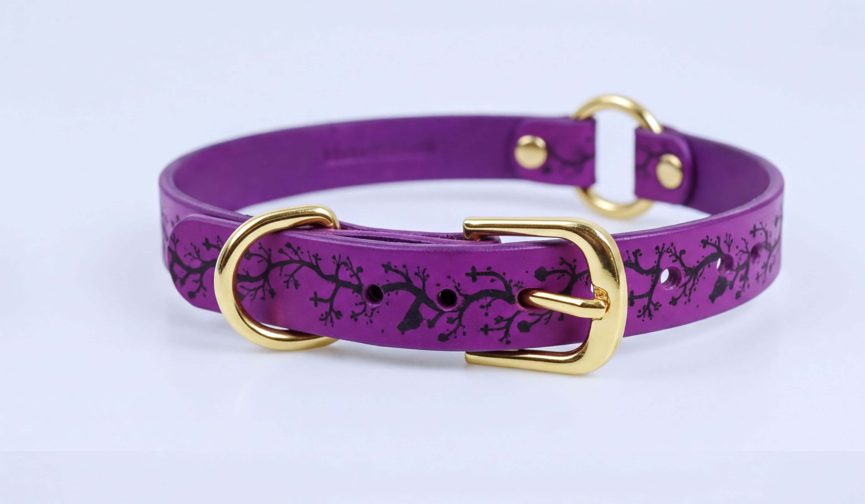 A purple leather dog collar with a gold buckle and a black tree design on the front.