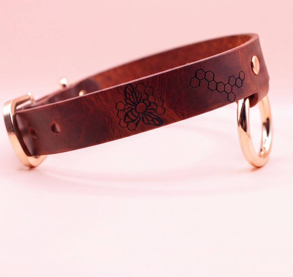 A brown leather dog collar with a floral design and two metal rings on the sides.