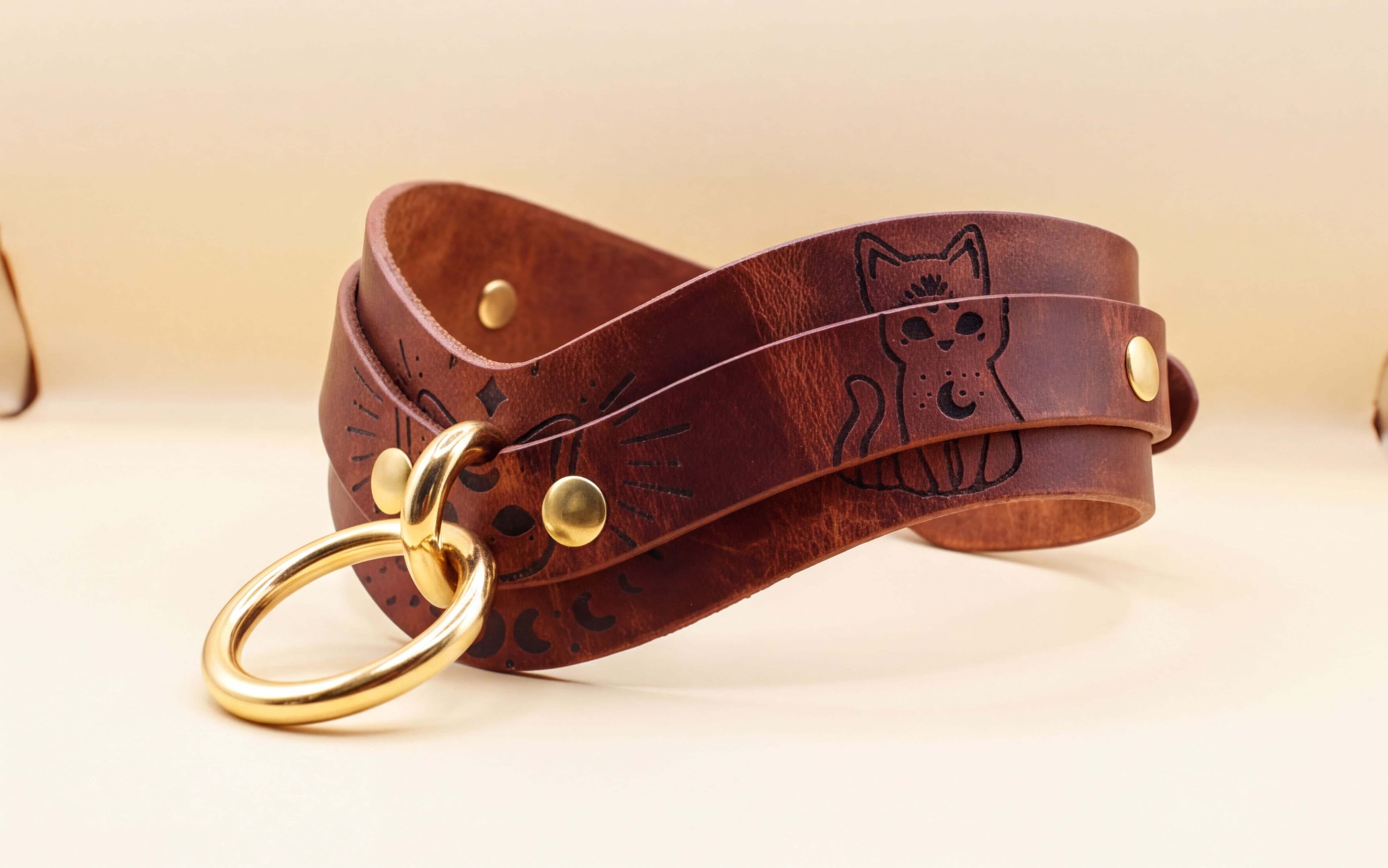 A brown leather choker necklace with a cat design and a gold ring.