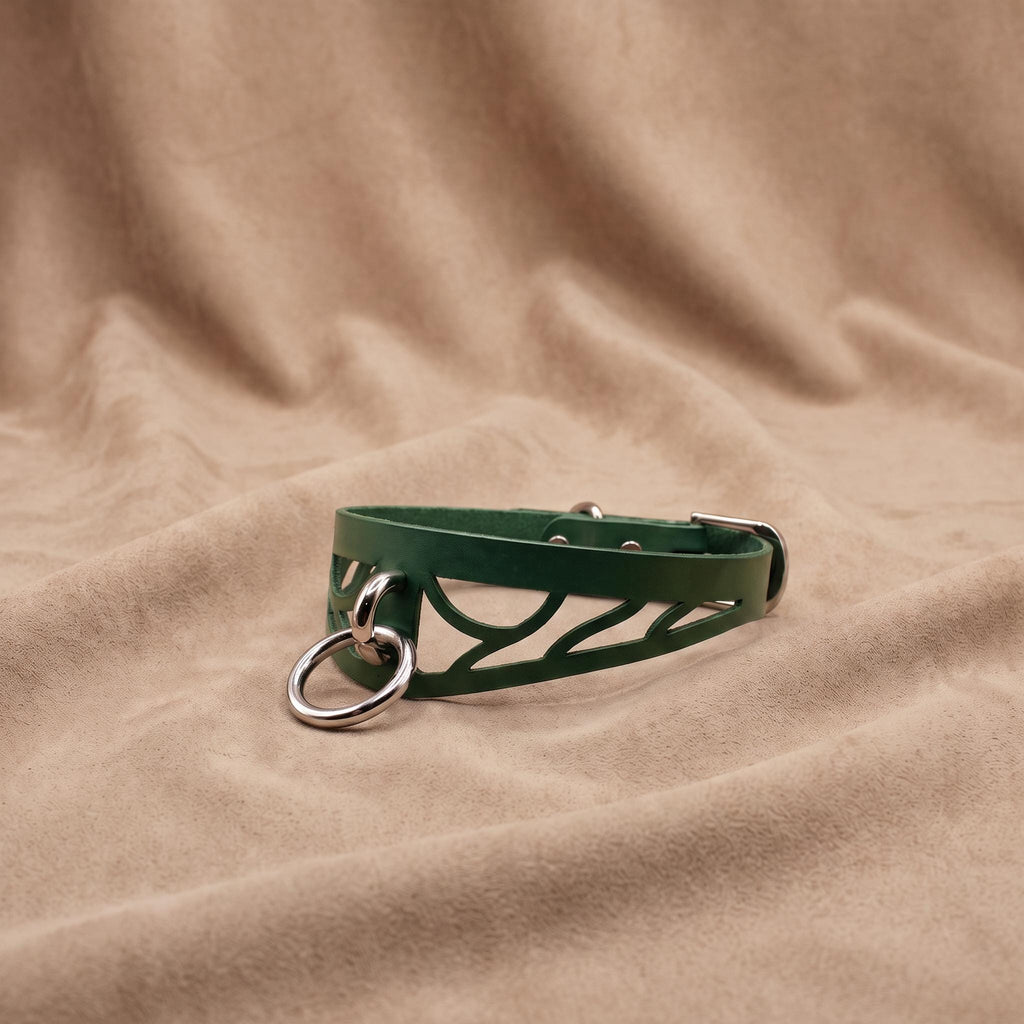 A green leather choker necklace with metal rings and a metal clasp is displayed on a beige fabric background.