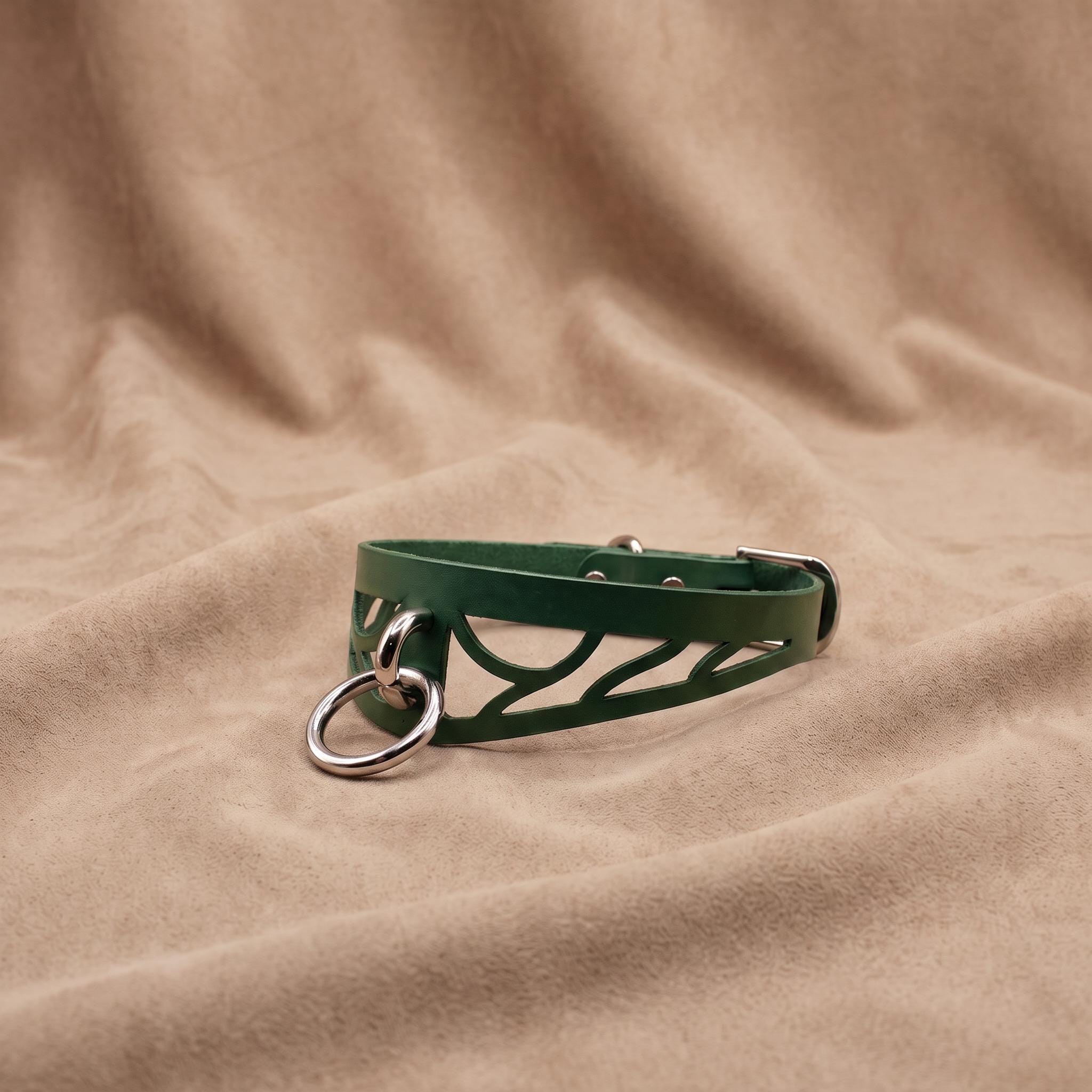 A green leather choker necklace with metal rings and a metal clasp is displayed on a beige fabric background.