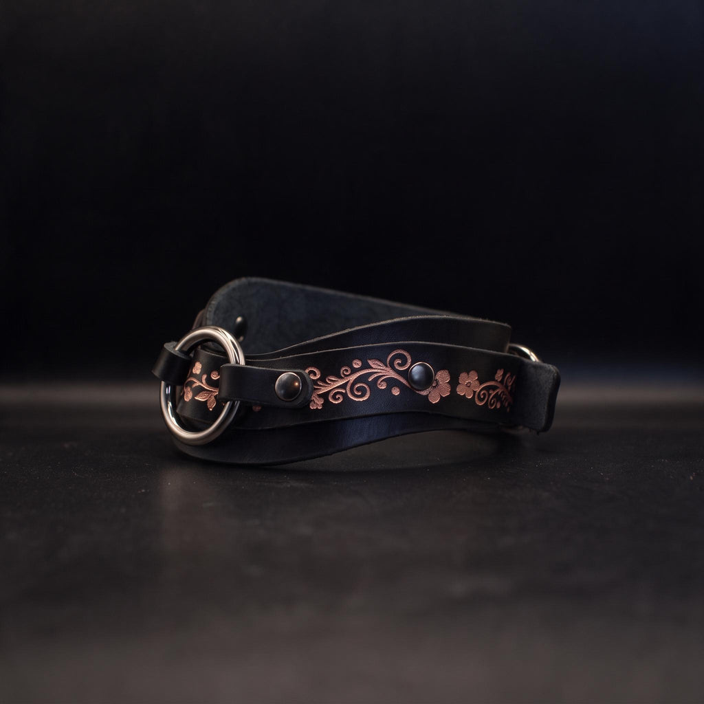 A black leather belt with a decorative floral pattern on the strap and a metal buckle.