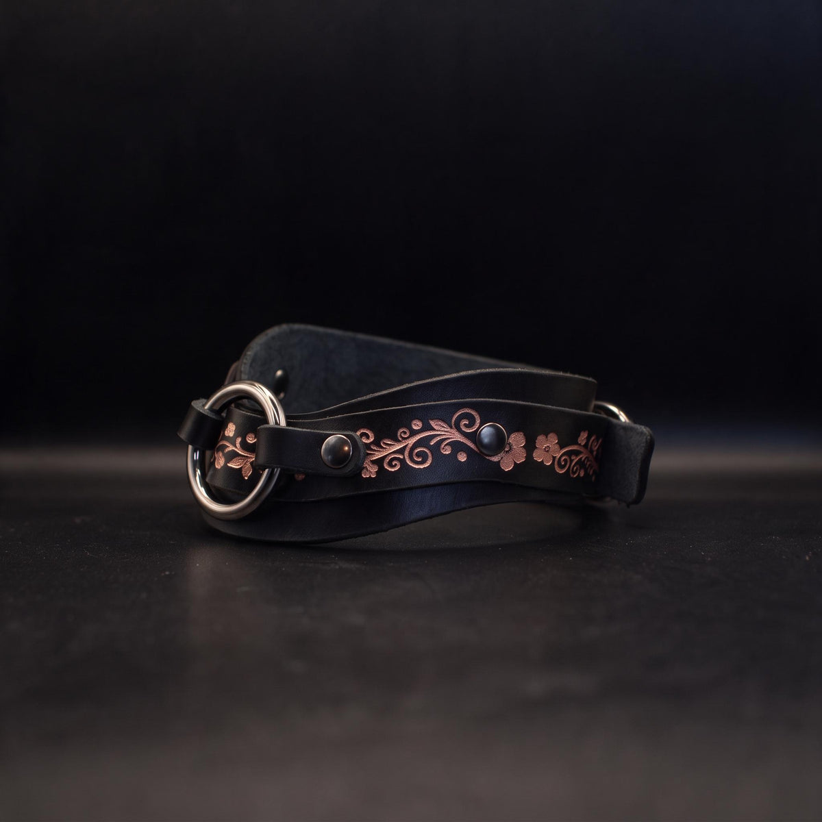 A black leather belt with a decorative floral pattern on the strap and a metal buckle.