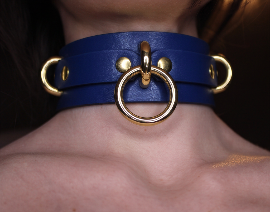 A close-up view of a person's neck wearing a blue leather choker necklace with gold-colored metal rings.