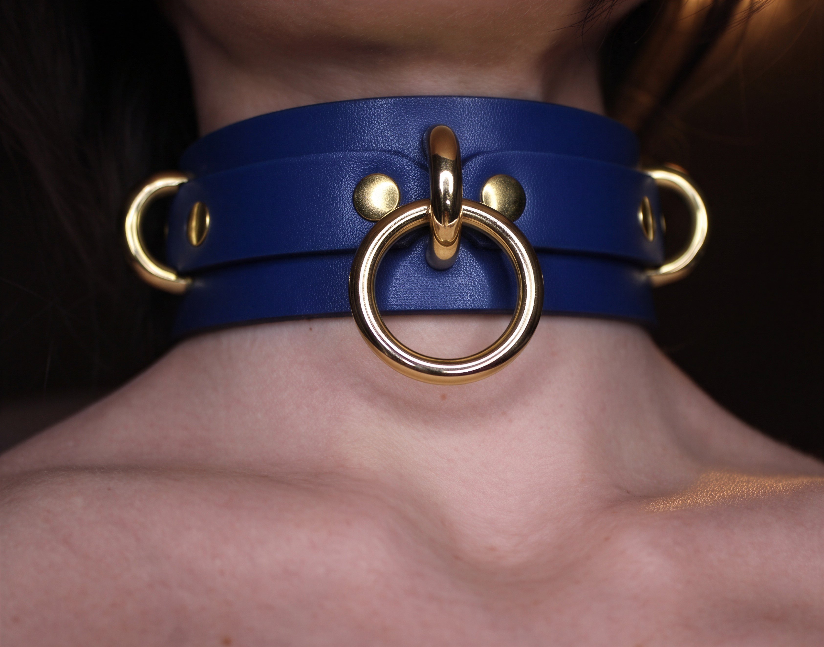 A close-up view of a person's neck wearing a blue leather choker necklace with gold-colored metal rings.