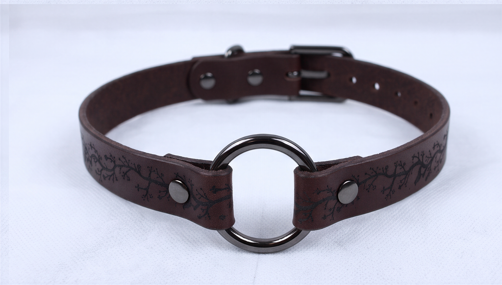 A brown leather choker necklace with a metal ring and a decorative pattern on the leather.