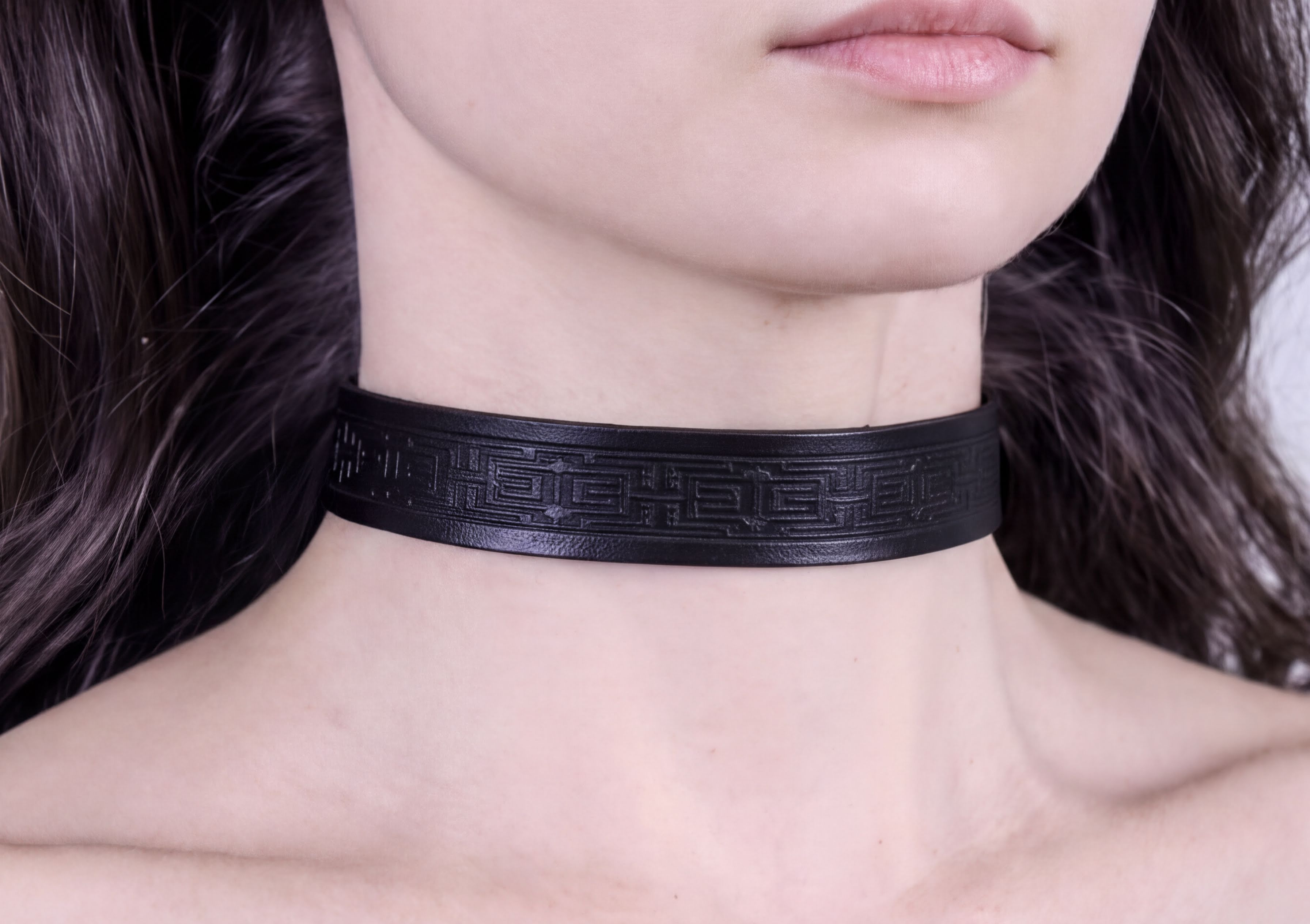 A close-up of a person's neck wearing a black choker necklace with an intricate design.