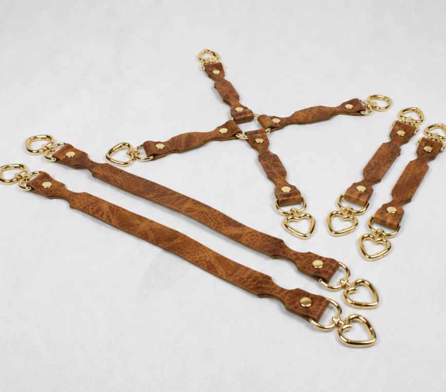 a collection of brown leather straps with gold hardware, including heart-shaped buckles, arranged on a white background.