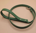 A green leather dog leash with a metal attachment is shown on a beige surface.