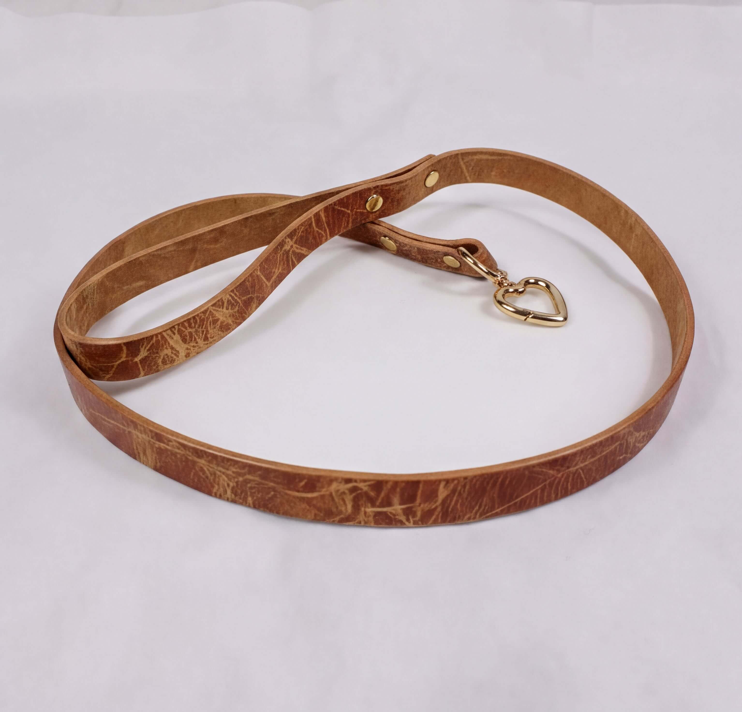 A brown leather leash with a gold-colored metal clasp and a heart-shaped charm attached.