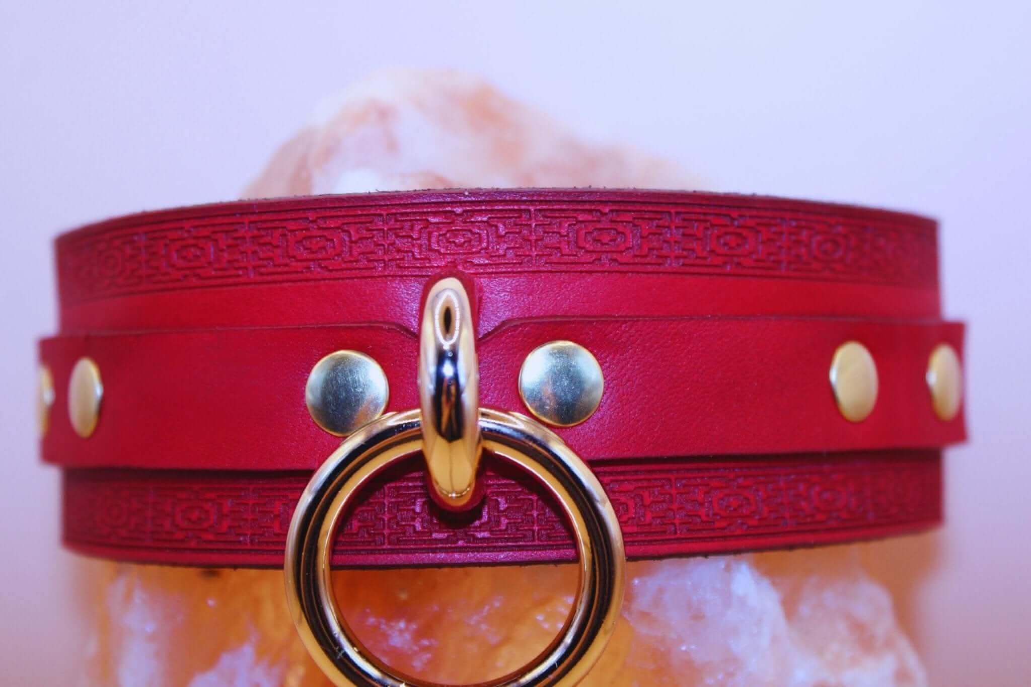 Crimson red BDSM collar with gold O-ring and embossed leather detail, ideal for submissive jewelry and bondage gear.
