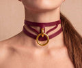 A close-up of a woman's neck wearing a burgundy leather choker necklace with a gold ring.