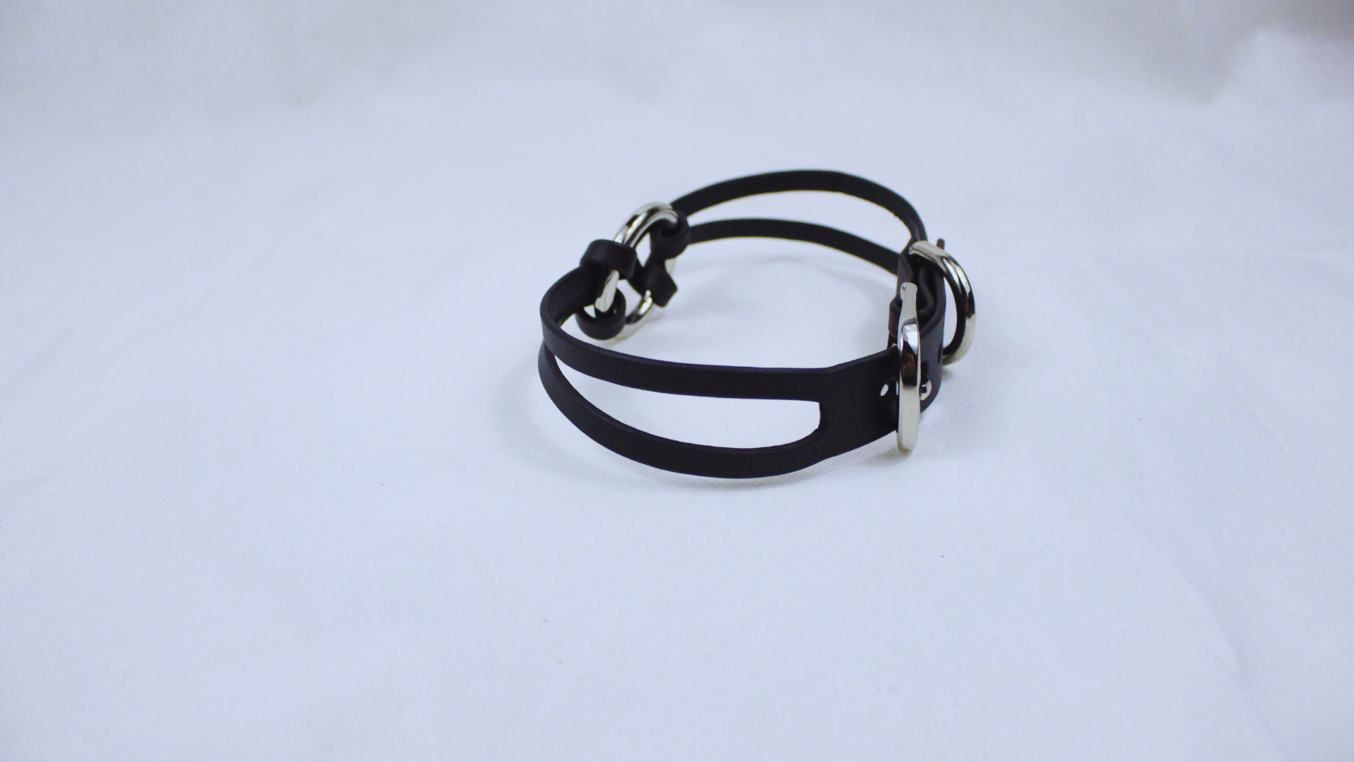 A black leather bracelet with silver buckles is shown against a white background.