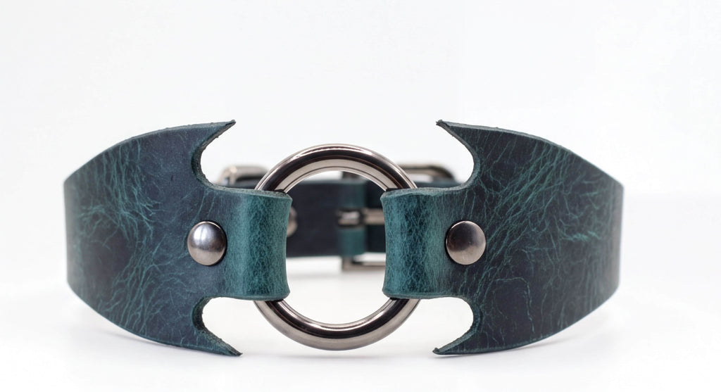 A close-up view of a green leather collar with a metal ring and two metal buttons.