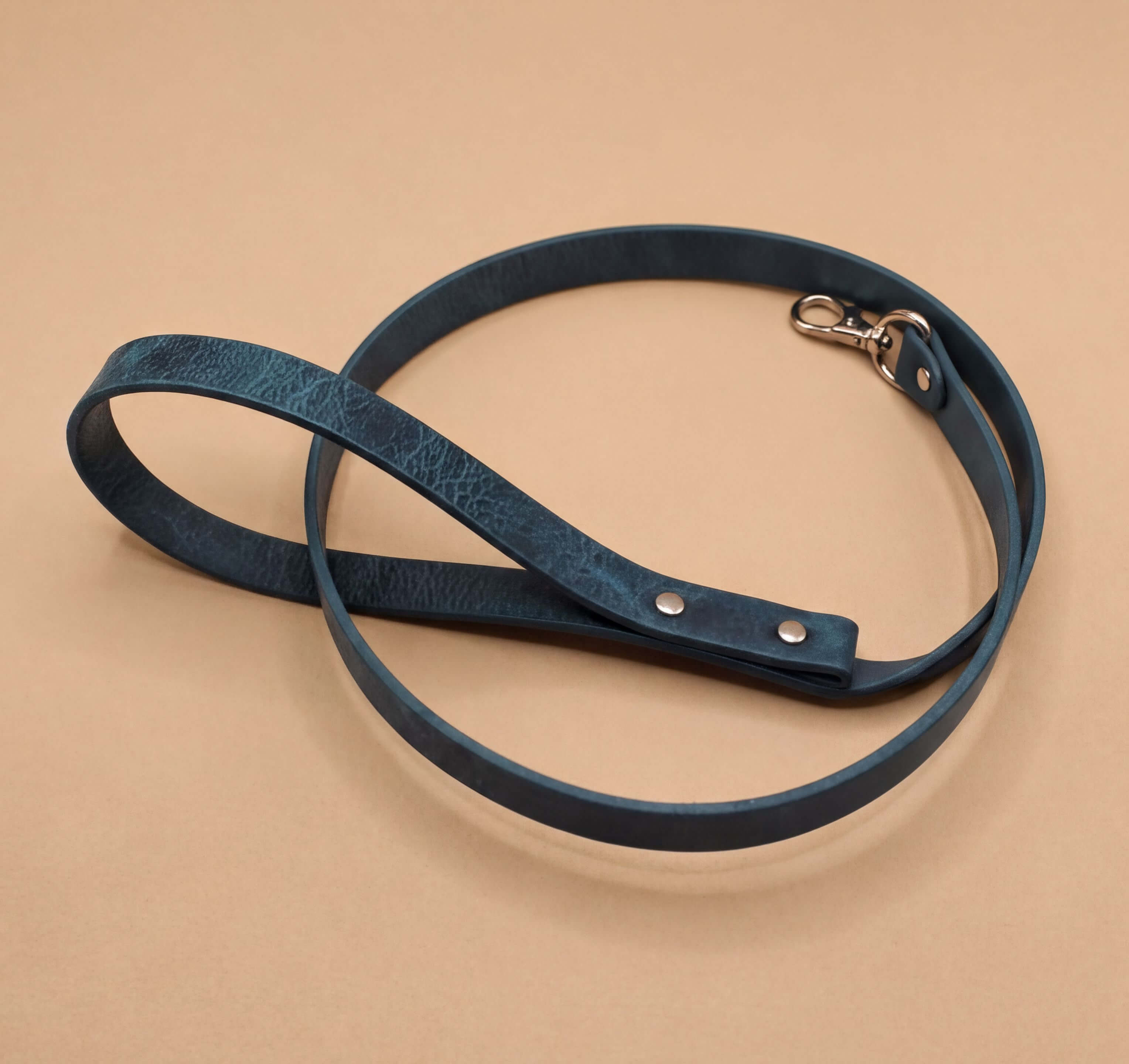 A dark blue leash with a metal clasp and buckle is shown against a beige background.