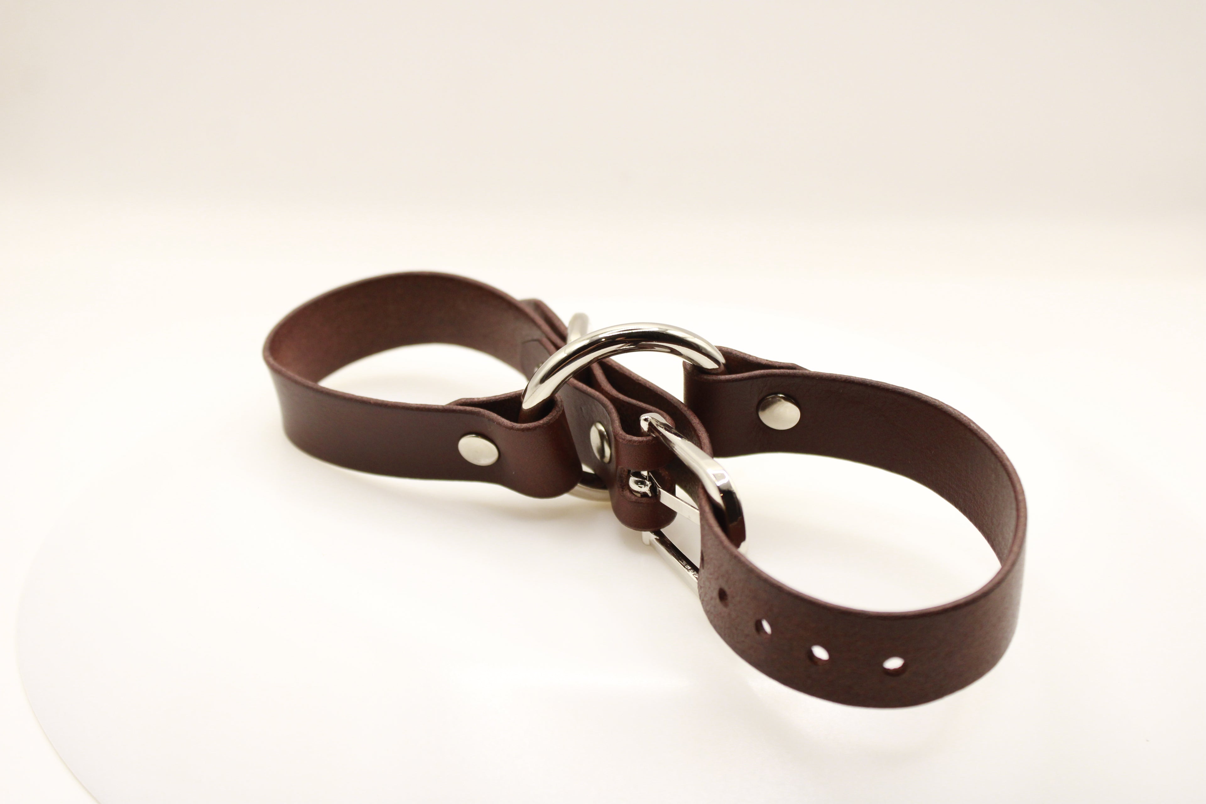 A brown leather strap with a metal buckle and holes, lying on a white surface.