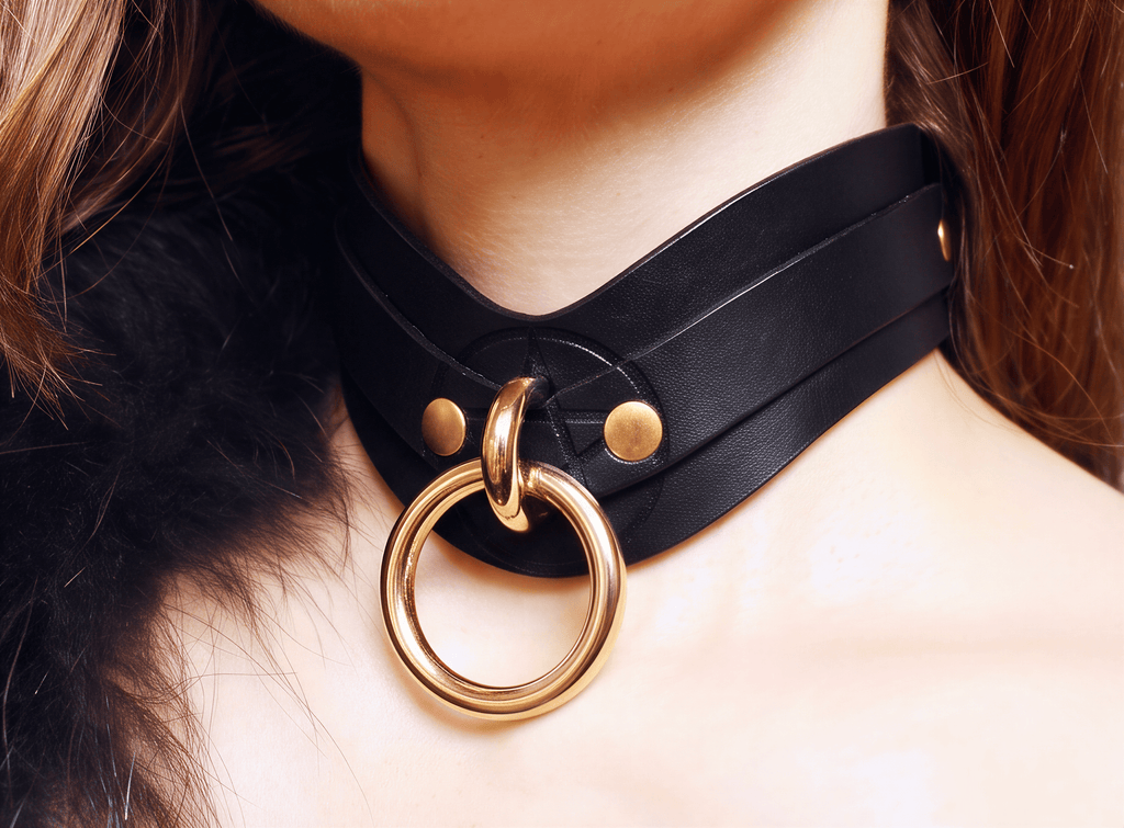 A close-up view of a person's neck and chest area wearing a black leather choker necklace with a gold ring.