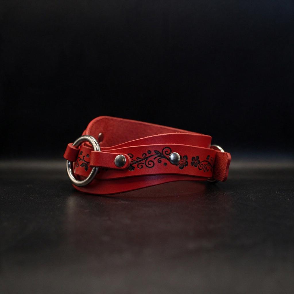 A red leather belt with a floral design on it, resting on a dark surface.